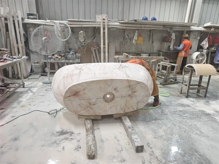 Stone craftsperson refining the machined Calacatta Rosa marble bathtub in the finishing workshop.