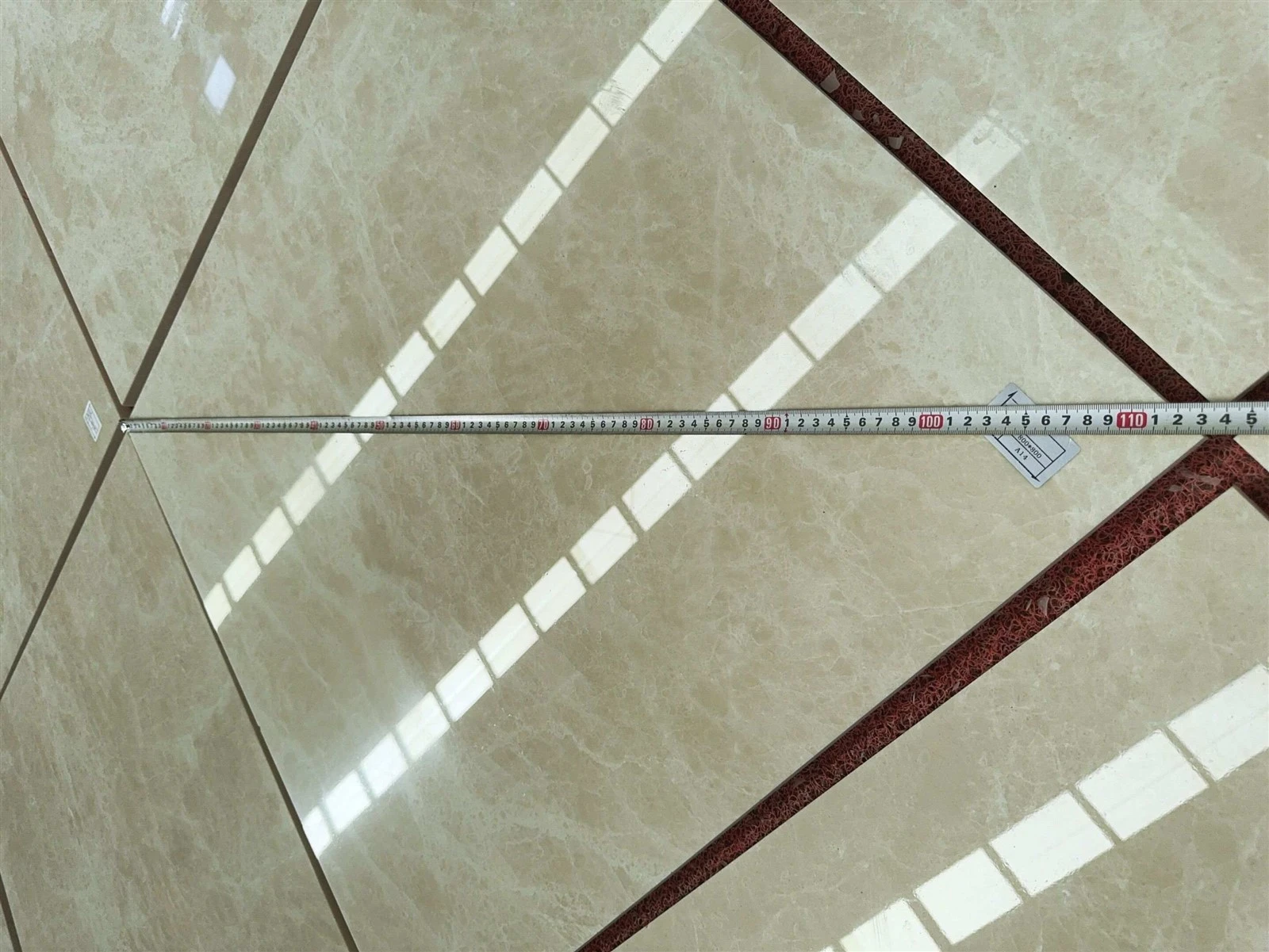 Factory dimension check of a polished Aran White Marble wall tile using a measuring tape beside the A14 identification label. Factory dimension check of a polished Aran White Marble wall tile using a measuring tape beside the A14 identification label.