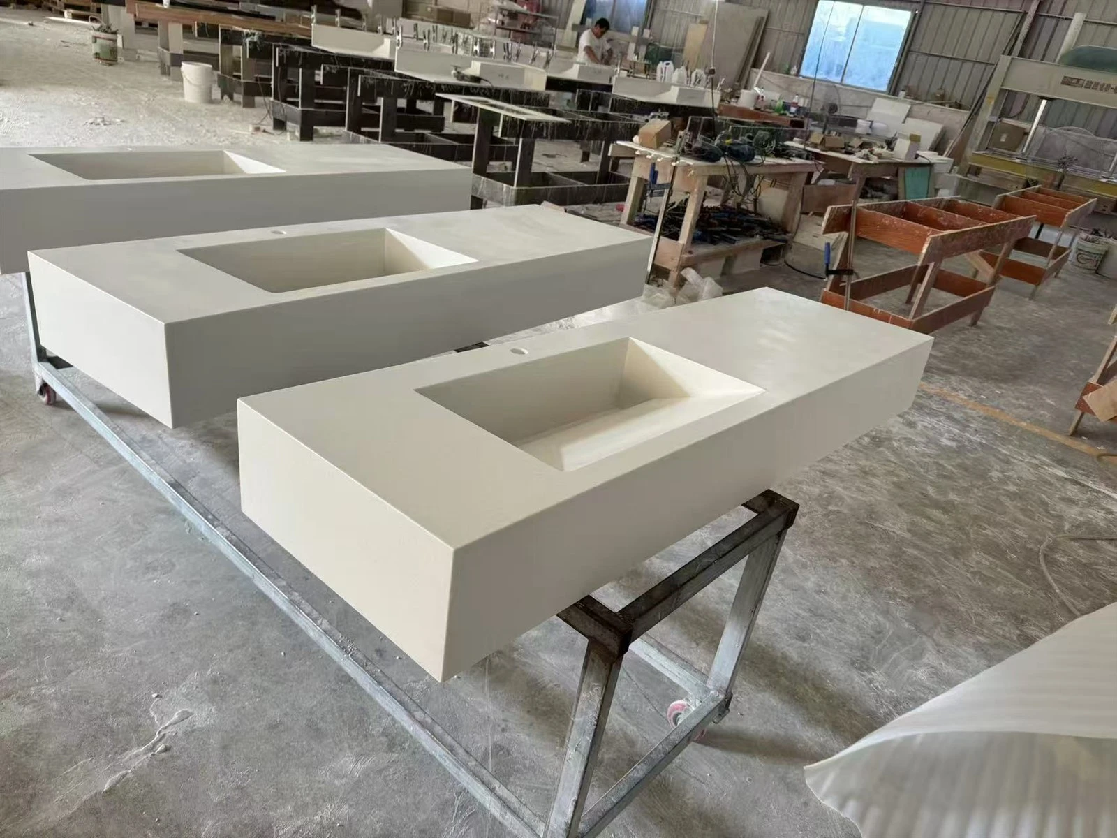Finished white acrylic countertops with integrated rectangular sinks arranged on fabrication stands for final inspection. Finished white acrylic countertops with integrated rectangular sinks arranged on fabrication stands for final inspection.